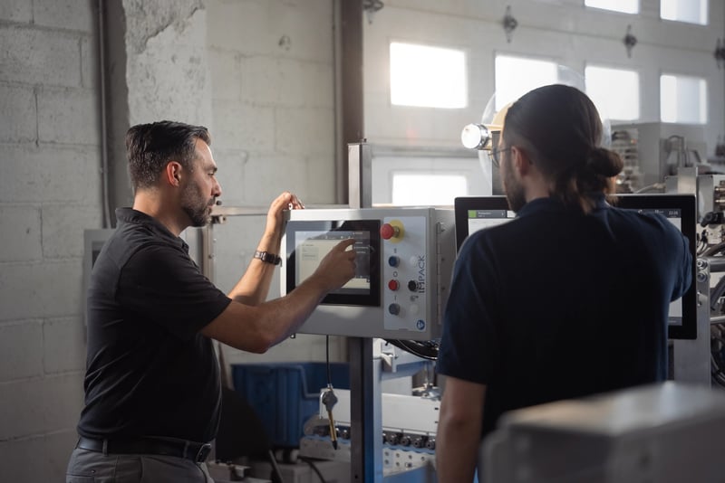 Two men look at an HMI screen. One makes selections by pushing buttons on the screen.