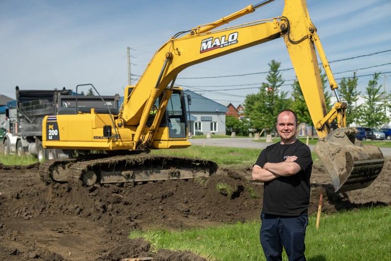 Michael Persechino, Plant Director at IMPACK, standing in front of the excavator at the construction site of the company's new facility beside its headquarters.